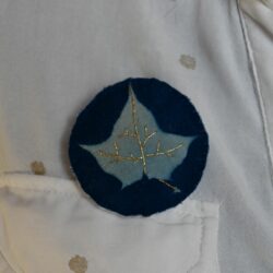 Une broche en tissu représentant une feuille d'érable révélé par le cyanotype et brodé au fil d'or