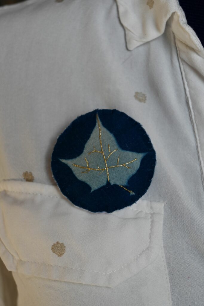 Une broche en tissu représentant une feuille d'érable révélé par le cyanotype et brodé au fil d'or