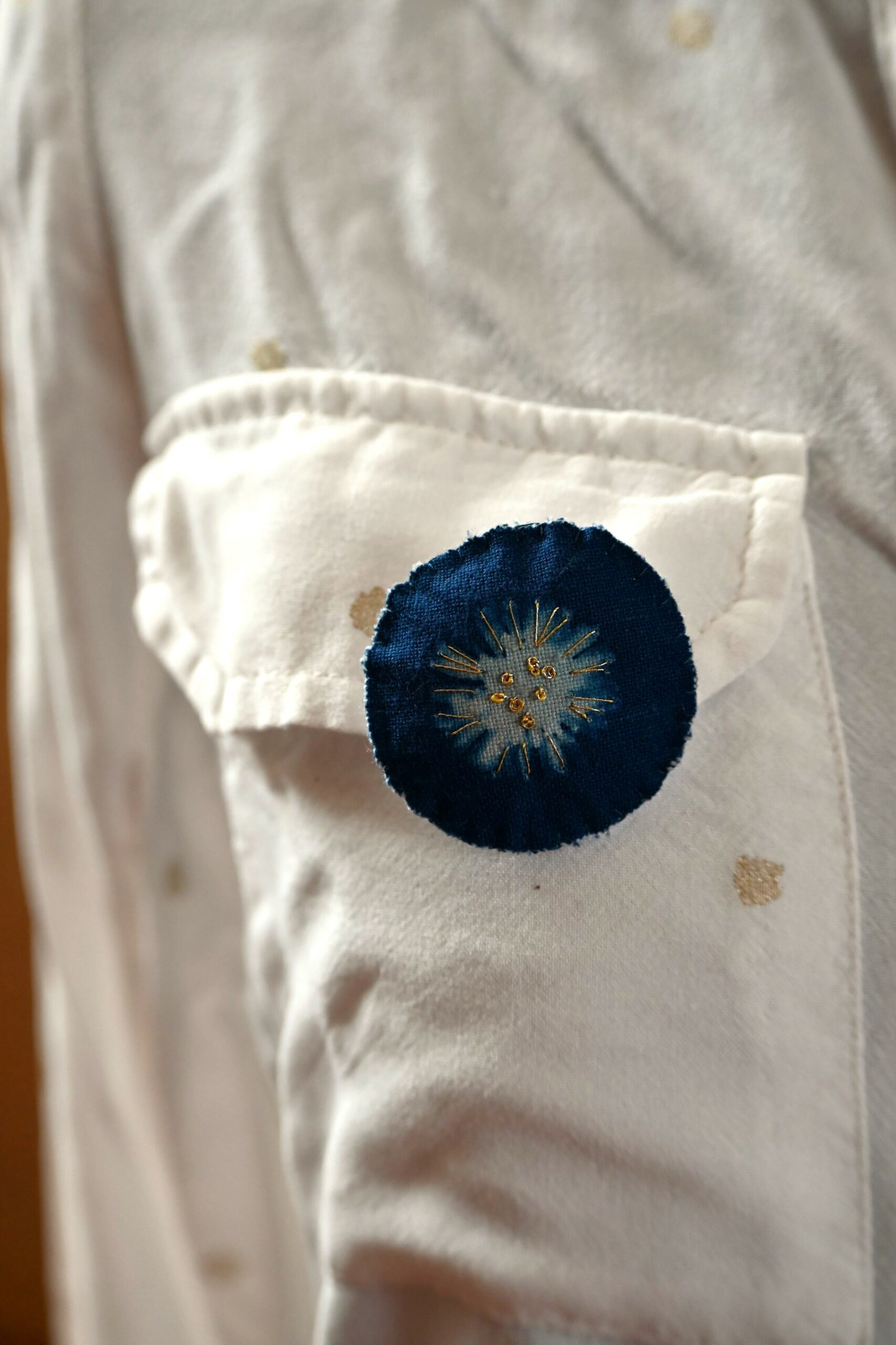 Broche cyanotype représentant une pâquerette, brodée de fil d'or et de perles dorées