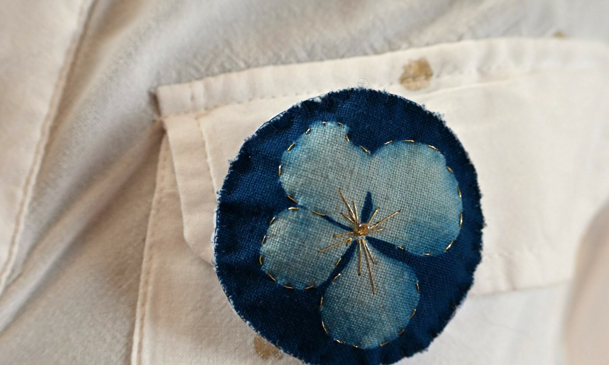 Broche impression cyanotype d'une fleur d'hortensia, brodée de fil d'or et perles dorées